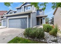 Two-story home with blue siding, a gray garage door, and river rock landscaping in front at 5453 S Quatar Ct, Aurora, CO 80015