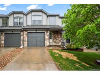 Charming townhome featuring stone accents, gray siding, attached garage, and landscaped front yard at 2002 E 102Nd Cir, Thornton, CO 80229