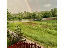 Rainbow over grassy backyard with red fence and trees at 15972 W 70Th Dr, Arvada, CO 80007