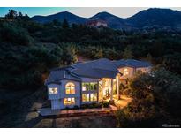 Aerial view of a two-story home with a tile roof and large windows nestled on a hillside with mountain views at dusk at 5799 Crestbrook Cir, Morrison, CO 80465