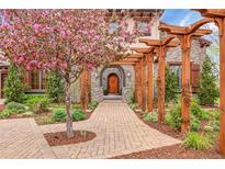 Inviting stone home featuring a beautiful flowering tree, lovely landscaping, and a welcoming covered walkway to the arched front door at 1423 E Fair Pl, Centennial, CO 80121