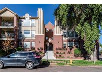 Attractive condominium building with red brick and tan facade, a car parked in front and greenery around the building at 1735 N Ogden St # 106, Denver, CO 80218