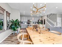 Bright dining room with a wooden table set, stylish chandelier, and a glimpse of the modern gray kitchen at 3778 Happyheart Way, Castle Rock, CO 80109