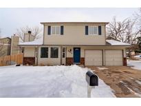 Charming two-story home with a blue door and a two car garage, complemented by a snow-covered front yard at 8012 S Cedar St, Littleton, CO 80120