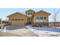 Charming tan house with well-kept landscaping, stone accents, and a concrete driveway with snow at 2600 Reserve Ct, Erie, CO 80516