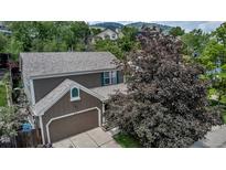A two-story brown home features an attached two-car garage, manicured lawn, and a large tree in the front yard at 573 Entrada Dr, Golden, CO 80401