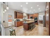 Open kitchen boasts granite counters, island with seating, stainless appliances, tile flooring, and ample cabinet space at 9451 S Hackberry Ln, Highlands Ranch, CO 80129