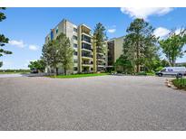 View of the building featuring an asphalt parking lot, exterior landscaping, and an array of green trees at 13902 E Marina Dr # 303, Aurora, CO 80014