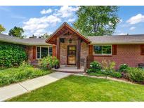 Charming brick home featuring a covered front porch with wood accents and lush landscaping at 2775 Crabapple Rd, Golden, CO 80401