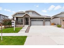Charming home featuring a stone-accented entrance, gray siding, a three-car garage, and a well-manicured lawn at 17247 E 103Rd Ave, Commerce City, CO 80022