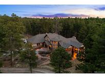 Stunning exterior view of the stone home nestled amongst lush trees with a colorful dusk sky at 10231 Democrat Rd, Parker, CO 80134
