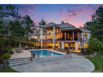 An expansive backyard featuring a pool, fire pit, string lights, stone accents, and elegant two-story home at dusk at 10914 Remmick Ridge Rd, Parker, CO 80134