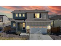 Charming two-story home featuring mixed siding, stone accents, an attached two-car garage, and beautiful sunset sky at 17947 E 95Th Ave, Commerce City, CO 80022