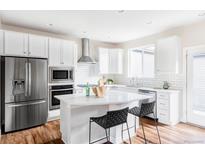 Bright kitchen features white cabinetry, stainless steel appliances, island with bar seating, and light countertops at 11488 E 25Th Dr, Aurora, CO 80010
