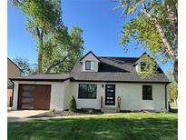 Charming Cape Cod-style home with white brick, black trim, and a modern wood-toned garage door at 1980 S Kearney Way, Denver, CO 80224