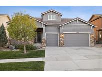 Charming gray home featuring a well-maintained lawn, stone accents, and a three-car garage at 15995 Humboldt Peak Dr, Broomfield, CO 80023