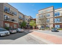 Beautiful condo complex with tan and brick facade, balconies, sidewalks, and parking on a sunny day at 5677 S Park Pl # A102, Englewood, CO 80111