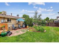 Landscaped backyard featuring a stone patio with umbrella, flower garden, and mature trees at 11835 W 37Th Pl, Wheat Ridge, CO 80033