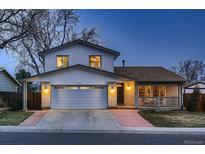 Charming home featuring an attached two-car garage, covered front porch, and well-maintained landscaping at dusk at 8485 W 74Th Dr, Arvada, CO 80005