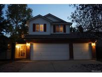 Charming two-story home with a brick-accented three-car garage and red shutters, illuminated by warm, inviting lights at 11302 W Prentice Dr, Littleton, CO 80127