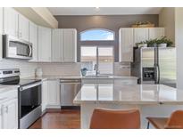 Modern kitchen features stainless steel appliances, white cabinets, granite countertops, and arched window with view at 2261 Alpine Dr, Erie, CO 80516