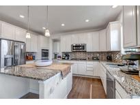 Bright kitchen features stainless steel appliances, granite countertops, island, and a tile backsplash at 8255 S Vandriver Way, Aurora, CO 80016