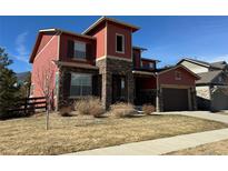 Attractive two-story home featuring red siding, a stone pillar entrance, and a well-maintained lawn at 11999 S Stroll Ln, Parker, CO 80138