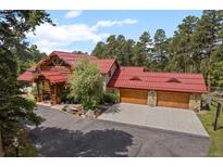 Beautiful log home with red roof and three-car garage nestled in lush greenery at 23076 Oehlmann Park Rd, Conifer, CO 80433