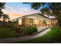 Charming brick home with a covered front porch and well-maintained landscaping at dusk at 1432 Xanthia St, Denver, CO 80220