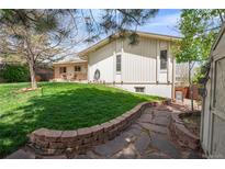 Beautifully landscaped backyard with lush green grass, a stone patio, and mature trees providing shade and privacy at 12662 W Asbury Pl, Lakewood, CO 80228