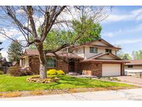 Charming two-story home with a brick facade, well-manicured lawn, mature tree, and attached two car garage at 11131 W Oregon Pl, Lakewood, CO 80232