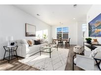 Bright living room featuring a white sofa, glass coffee table, modern rug, and dining area with abundant natural light at 2140 Santini Trl # D, Littleton, CO 80129