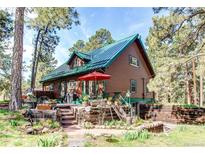 Charming log home with a green metal roof, deck, and inviting outdoor space surrounded by tall trees at 5030 Cedar Way, Elizabeth, CO 80107