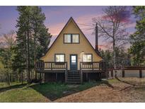 Charming A-frame cabin featuring a cozy front porch and nestled among mature trees at dusk at 9185 Jill Dr, Conifer, CO 80433