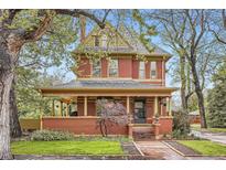 Stunning red brick two-story home featuring a covered front porch, landscaped yard, and charming architectural details at 835 Niagara St, Denver, CO 80220