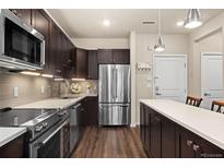Modern kitchen featuring stainless steel appliances, dark cabinets, quartz countertops, and hardwood floors at 155 S Monaco Pkwy # 114, Denver, CO 80224