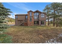 Charming brown two-story home featuring a stone chimney and large windows at 7082 Silverhorn Dr, Evergreen, CO 80439