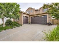 Tan two-story home featuring a three car garage, tidy lawn, and lovely shade trees at 4965 Huntwick Pl, Highlands Ranch, CO 80130