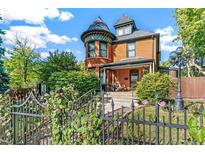 Charming Victorian home with a turret, covered porch, and wrought iron fence, surrounded by lush landscaping at 3015 Lowell Blvd, Denver, CO 80211