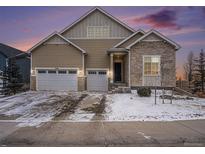 Charming home featuring a three car garage, stone accents, complemented by snowy landscaping and twilight sky at 8440 Rush Creek Ave, Littleton, CO 80125