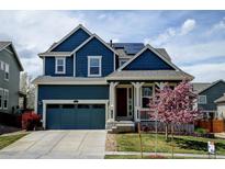 Charming blue two-story home featuring a covered front porch, blue garage door, and a well-manicured lawn at 10733 Salida St, Commerce City, CO 80022