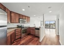 Modern kitchen featuring stainless steel appliances, granite countertops, and rich wood cabinetry and flooring at 100 Park Ave # 907, Denver, CO 80205