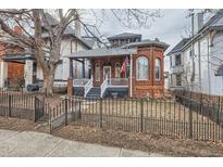 Charming brick home featuring a welcoming front porch and a classic black wrought iron fence at 1229 Josephine St, Denver, CO 80206