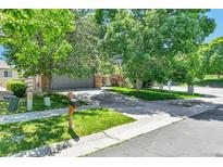 Charming home featuring a lush lawn and mature trees, leading to a gray two-car garage and driveway at 14944 E Archer Cir, Aurora, CO 80012