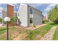 Corner unit townhome featuring vinyl siding, a brick chimney, green lawn, and a rock path at 3341 S Monaco Pkwy # A, Denver, CO 80222