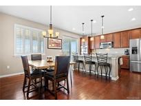 Charming dining area featuring hardwood floors and stylish lighting fixture open to the kitchen and breakfast bar at 16525 Sanford St, Mead, CO 80542