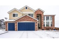 Two-story brick home with a three-car garage and snowy front yard at 1035 Cryolite Pl, Castle Rock, CO 80108