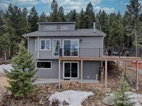 Contemporary home featuring a spacious deck, gray siding, a walkout basement, and surrounded by a lush forest setting at 31932 Steven Way, Conifer, CO 80433