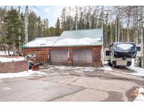 Large, rustic wooden garage with two bays, snow-covered roof, and an RV parked outside at 9061 N Rex Ln, Conifer, CO 80433
