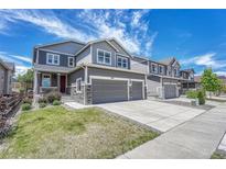Charming two-story home with a manicured lawn, gray siding, stone accents, and a two-car garage at 10887 Endeavor Dr, Parker, CO 80134